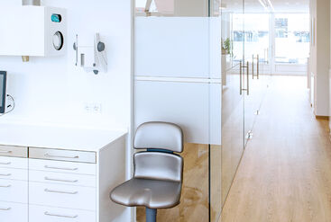 Hallway in a dentist's office, wooden floor and white furniture; in the foreground a swivel chair.